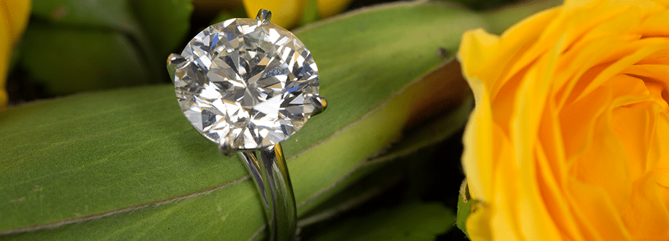 diamond ring wrapped around leaves of a flower, and yellow roses in background