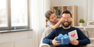 young girl holding her hands over her father's eyes, surprising him with a father's day gift