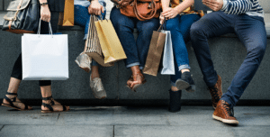 shoppers sitting outdoors on a low cement wall holding shopping bags
